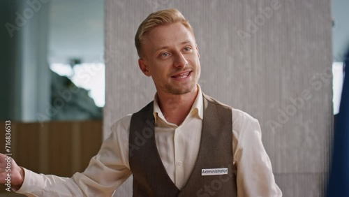 Friendly concierge talking guests at reception closeup. Smiling man in uniform photo