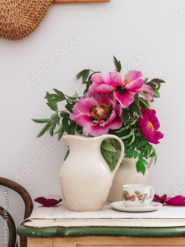 Pink and purple peonies in a jug and a cup on a table. Still life with flowers