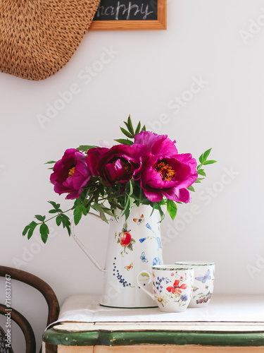 Purple peonies in a jug and cups on a table. Beautiful spring morning scene