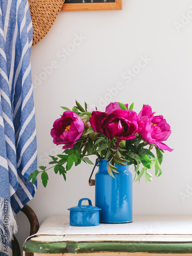 Kitchen table with beautiful flowers from the garden. Purple peonies in a blue metal can. 