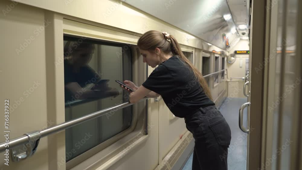 Modern woman walks down the corridor of a compartment car. She stops at the window and uses her smartphone Modern woman walks down the corridor of a compartment car. She stops at the window and uses her smartphone