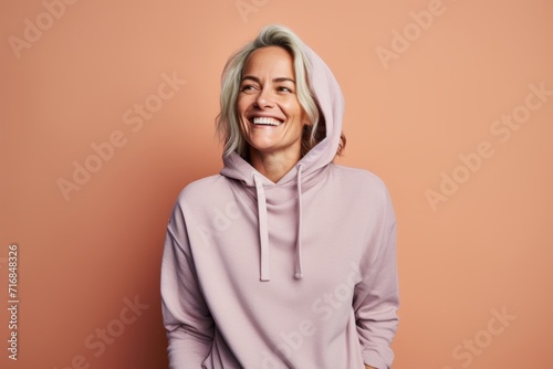 Portrait of a happy woman in her 40s sporting a comfortable hoodie against a solid pastel color wall. AI Generation © CogniLens