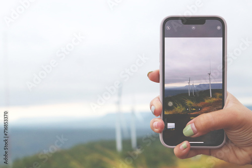 Woman hand using smartphone taking photo of windmill landscape view.