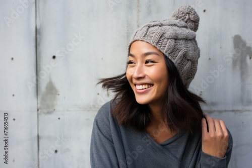 Portrait of a joyful asian woman in her 40s donning a warm wool beanie against a bare concrete or plaster wall. AI Generation