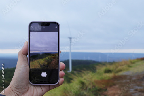 Woman hand using smartphone taking photo of windmill landscape view.