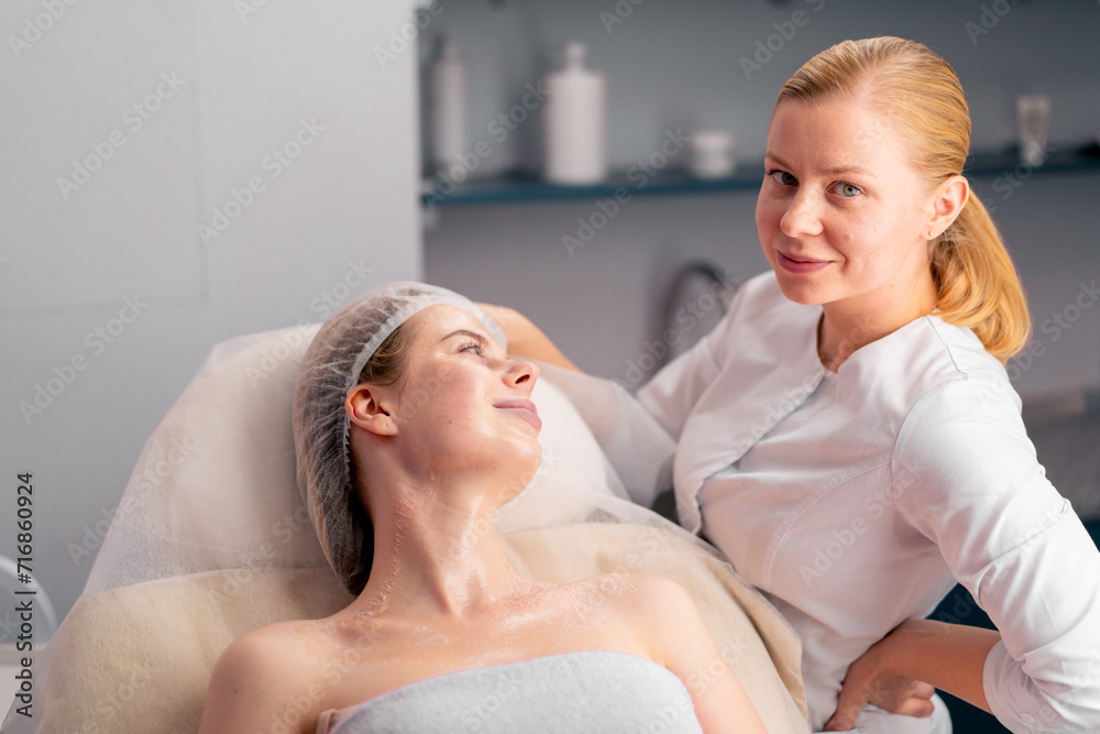 a cosmetologist advises a satisfied client during a skin care procedure in a beauty salon