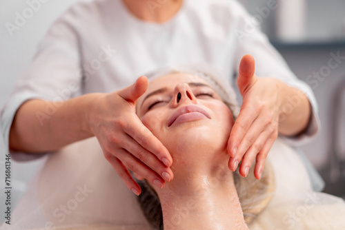 close-up beautician rubs the serum into the client's face in the salon with massaging movements