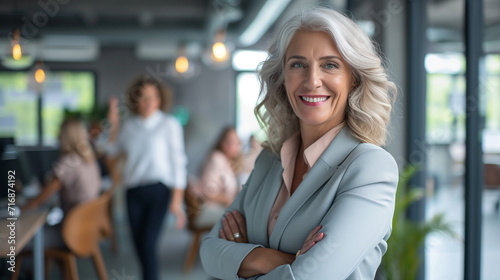 Smiling middle aged beautiful female business person in front of cheerful co-workers in office