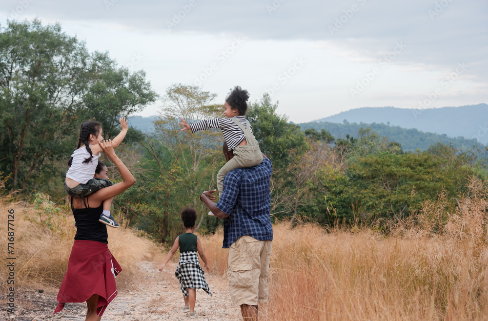 Happy African American family with adorable children in weekend vacation camping outdoors in countryside, father carry daughter on shoulder walking around in forest with fun, bonding relationship