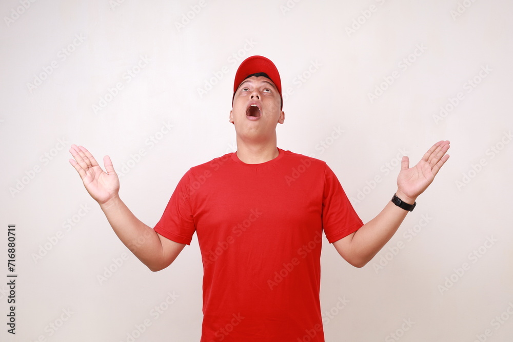 Wow excited Handsome young asian courier standing while getting something from above against white background