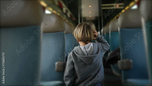 Back of little boy walking in train corridor while traveling inside high-speed transportation in motion. Child exploring vacant passenger seats