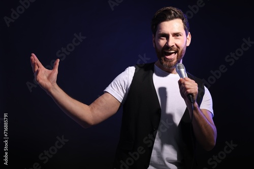 Handsome man with microphone singing on dark blue background