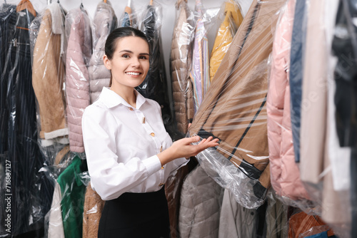 Dry-cleaning service. Happy worker choosing clothes from rack indoors