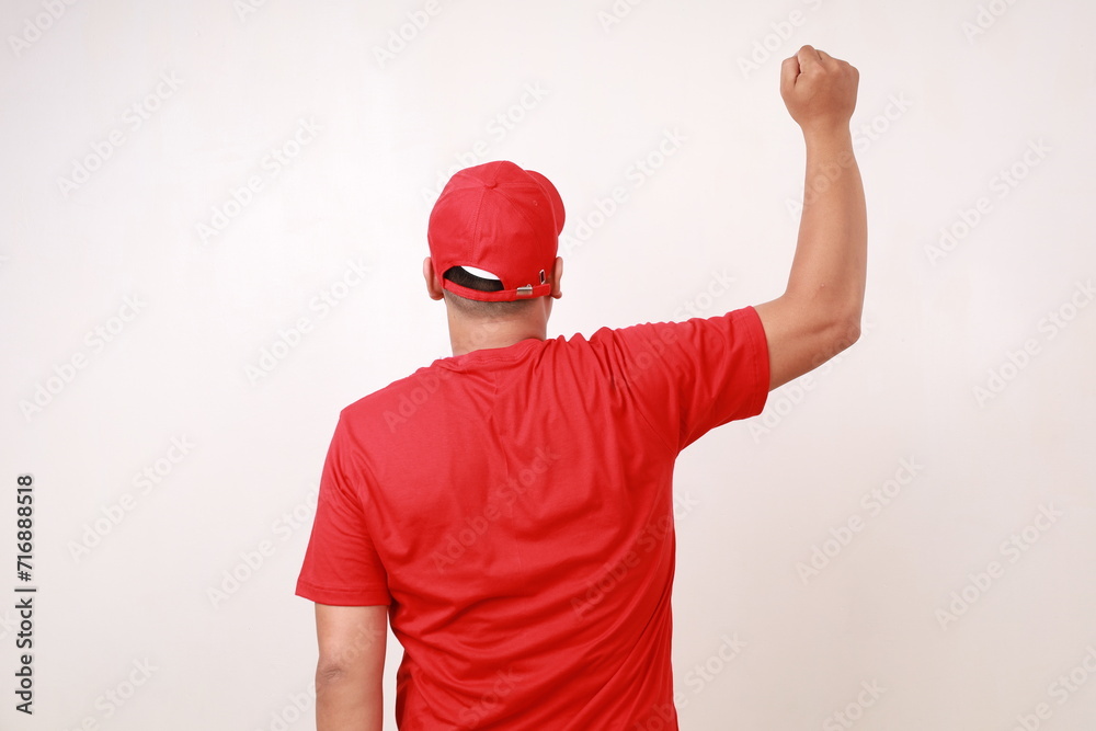Back view of Asian delivery guy employee man in red standing while lifting clenched hand, isolated on white background Back view of Asian delivery guy employee man in red standing while lifting clenched hand, isolated on white background