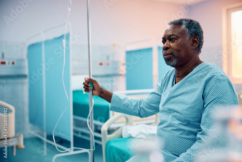 Fotografiet Pensive black senior man with IV drip recovering in hospital ward