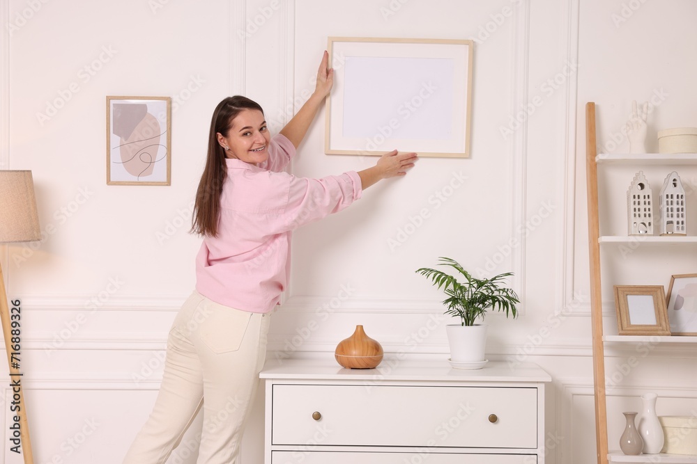 Woman hanging picture frame on white wall at home Woman hanging picture frame on white wall at home