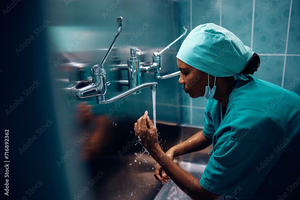 Black female doctor washing her hands before surgery in hospital. - obrazy, fototapety, plakaty 