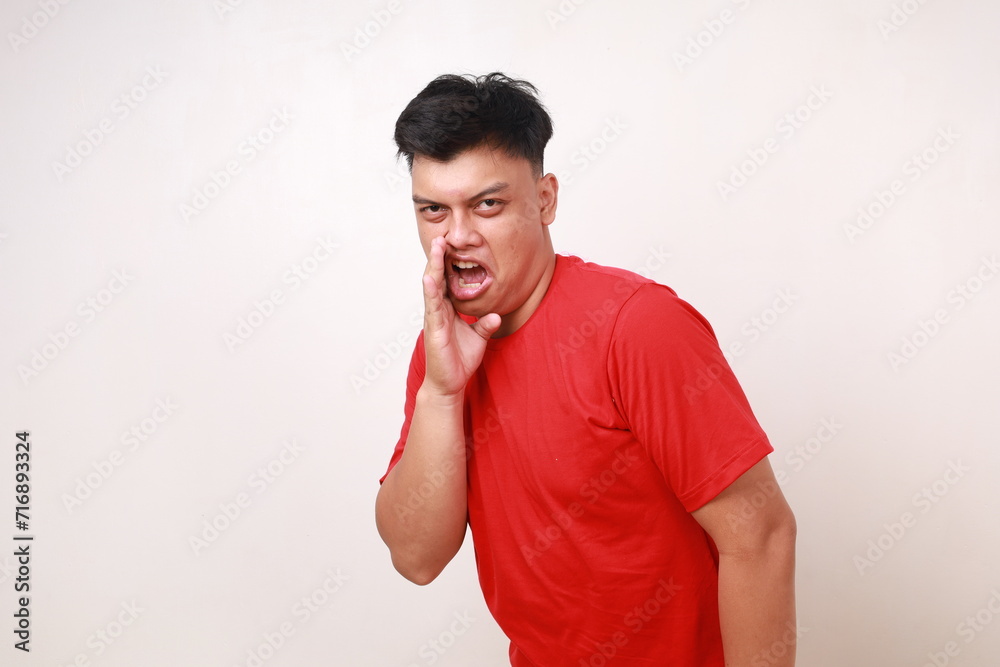 Funny young asian man in red is whispering some secret gossip isolated on white background Funny young asian man in red is whispering some secret gossip isolated on white background