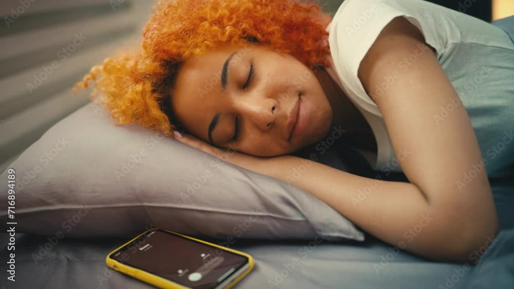 Young woman sleeps in bed, ignoring call from boss in the morning, late for work