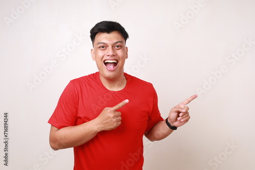 Wow funny expression of asian young man pointing sideways on empty space. Isolated on white