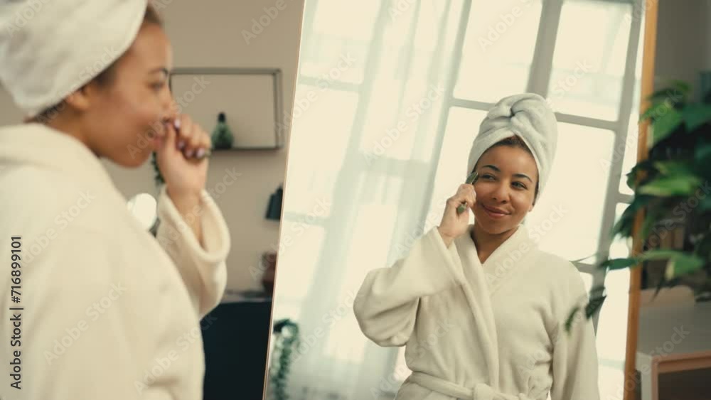 Pleased African American woman using face roller after a shower, home skincare Pleased African American woman using face roller after a shower, home skincare