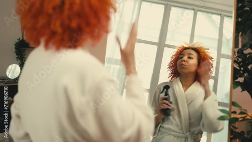 African American woman applying moisturizing spray on hair, heat protectant photo