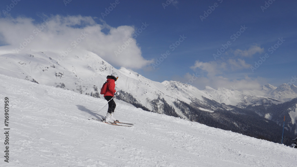 Active skier skiing down snowy slope in mountains at ski resort. Adrenaline is in blood from speed and breathtaking mountain scenery with snow capped summits and glaciers. Winter recreation and sports
