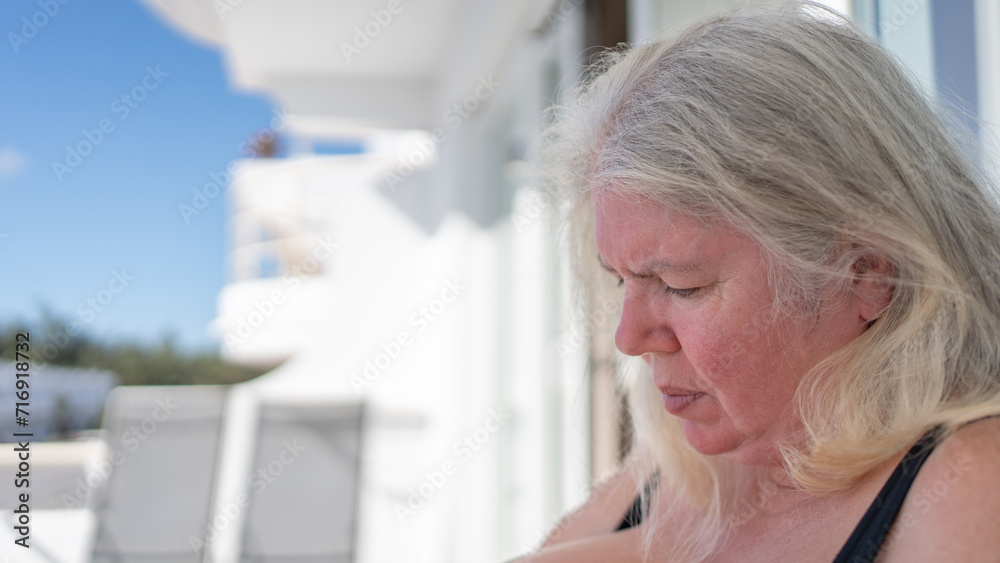 Older chubby women with gray hair and a bun are sitting in a swimsuit on a bright hotel balcony