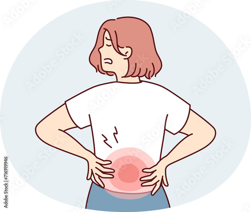 Woman stands with back to screen and holds on to red lower back after failing to lift heavy bag. Girl suffers from pain in spine needs massage or help of osteopath doctor.