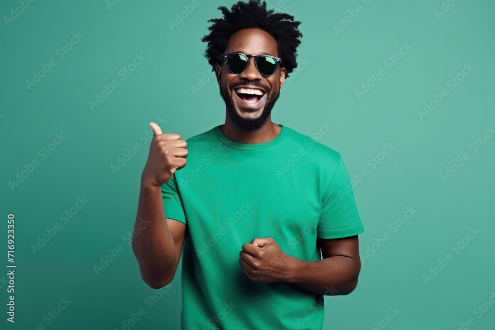 Portrait of toothy beaming nice African American man wear stylish t-shirt in eyewear hold smartphone arm in pocket isolated on green color background Portrait of toothy beaming nice African American man wear stylish t-shirt in eyewear hold smartphone arm in pocket isolated on green color background