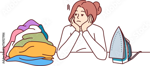 Pensive woman housewife sits near ironing board and iron, reflecting on lack of personal development. Housewife girl needs rest to recuperate and treat depression associated with burnout.