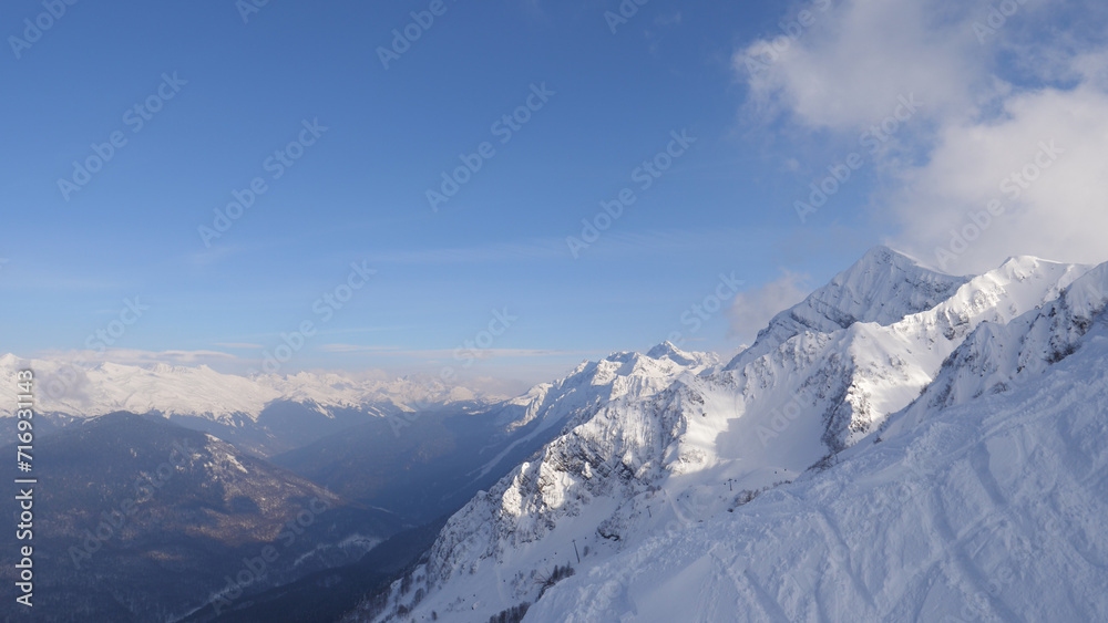 A picturesque landscape of mountains with snow capped peaks summits and glaciers on a sunny clear winter day. Shot in motion on ski lift