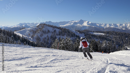 Woman skier skiing down snowy slope in mountains at ski resort in motion. Adrenaline in blood from speed and mountain landscape with snow capped peaks and glaciers. Winter healthy leisure and sports