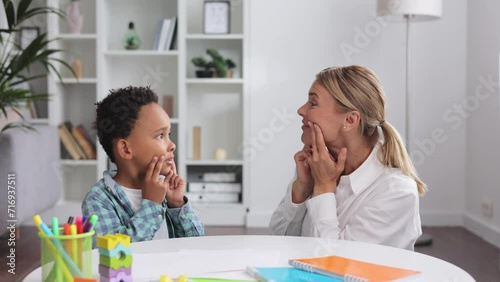 Cute little multiracial boy with speech problems practicing with occupational therapist, practicing and looking at mirror in office. The concept of childhood autism.