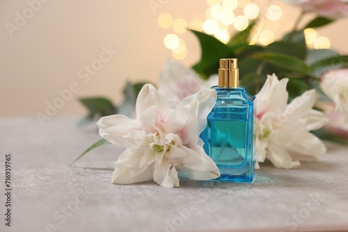 Bottle of perfume and beautiful lily flowers on table against beige background with blurred lights, closeup. Space for text