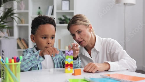 Assessment of mental development of children. Professional psychologist observes small multiracial boy playing with puzzle game, assessing his readiness for preschool. Exercises for kid with autism.