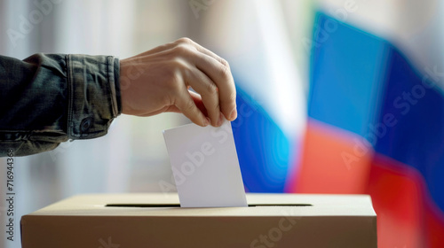 The hand of a voter dropping his vote into the ballot box. The concept of elections. The Russian flag is in the background. photo