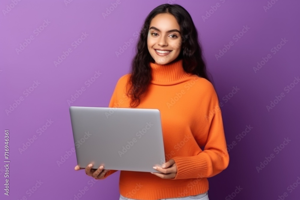 A girl with a laptop in an orange sweater on a solid purple background. A girl with a laptop in an orange sweater on a solid purple background.
