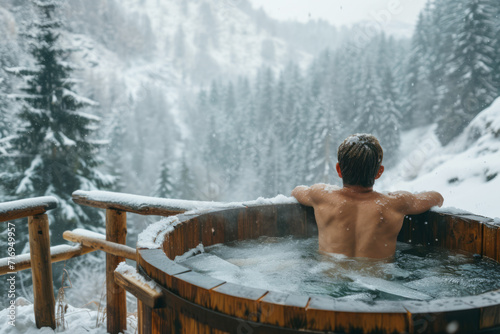 Back view of a man relaxing in a wooden outdoor ice bath amidst Winter forest covered in snow, wellness and cold water therapy benefits for health concept.