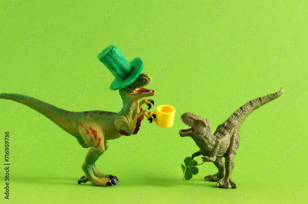 Fototapeta premium Two green dinosaurs in green hats with beer and clover leaf celebrating St. Patrick's day. Unusual festive card.