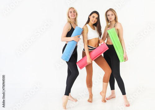 Group of sportive happy women holding yoga mats standing indoors