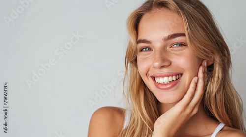 Smiling woman with a hand gently touching her face, displaying clear skin and a joyful expression.