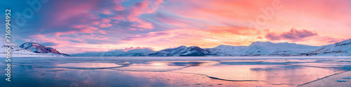 Vibrant extra wide panoramic sky. Frozen lake with mountain range in the horizon. Cinematic fantasy colorful sunset or sunrise sky. Shades of pink, orange, purple, red, yellow and blue. 