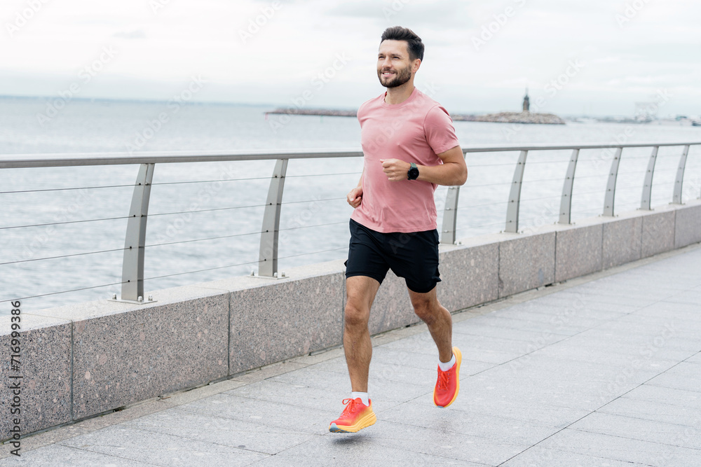 Active man running along a seaside promenade, with a distant view of a ...