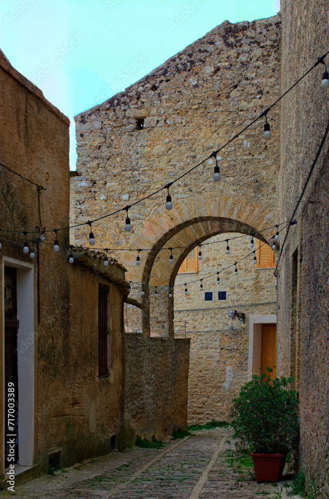 Picturesque view of typical narrow pedestrian medieval cobblestone street along ancient buildings in historical part of Erice village, Sicily, Italy. Travel and tourism concept