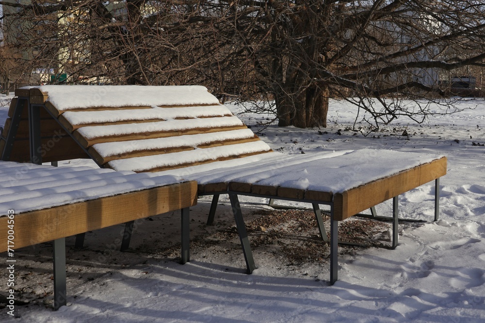 A snow-covered lounger in a city park.