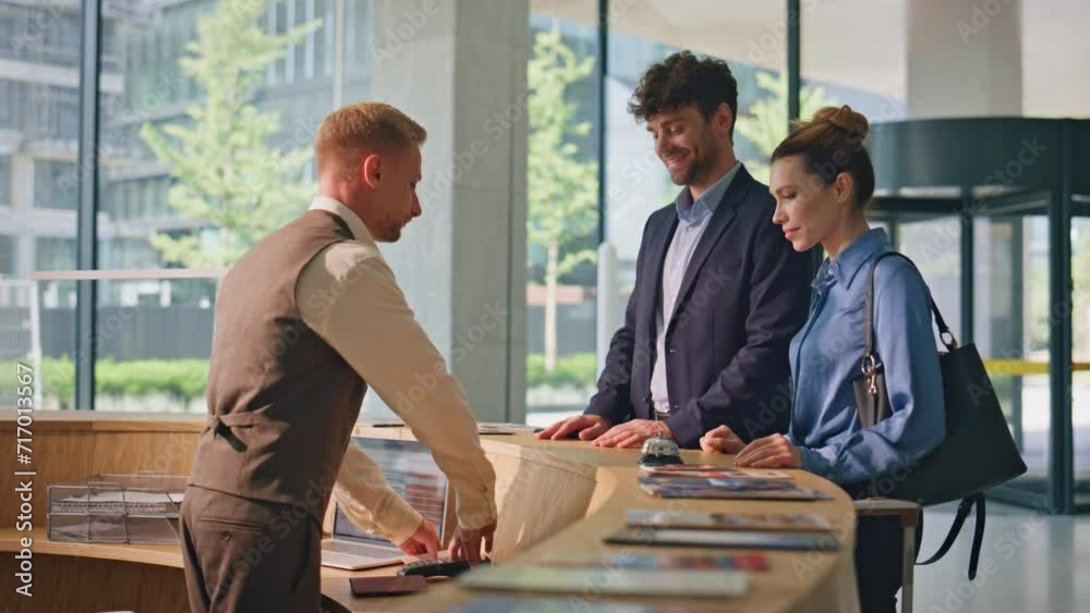 Hotel guests paying contactless with smartphone. Friendly receptionist check in