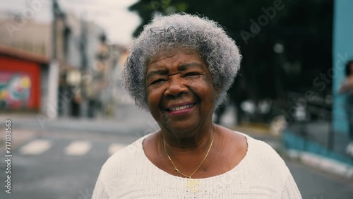 One happy black senior woman walking forward to camera in urban setting street. Gray hair elderly South American lady in 80s depicting active mature old age, portrait close-up photo