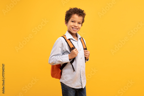 Cheerful schoolboy with backpack smiling at camera over yellow backdrop