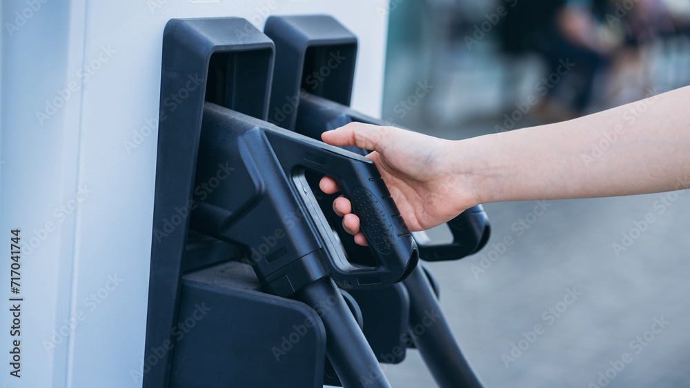 Close Up EV charging at station. Eco and clean energy concept. Hand of woman Charging Electric Vehicle. Convenient EV Charger in Hand. Close Up EV charging at station. Eco and clean energy concept. Hand of woman Charging Electric Vehicle. Convenient EV Charger in Hand.